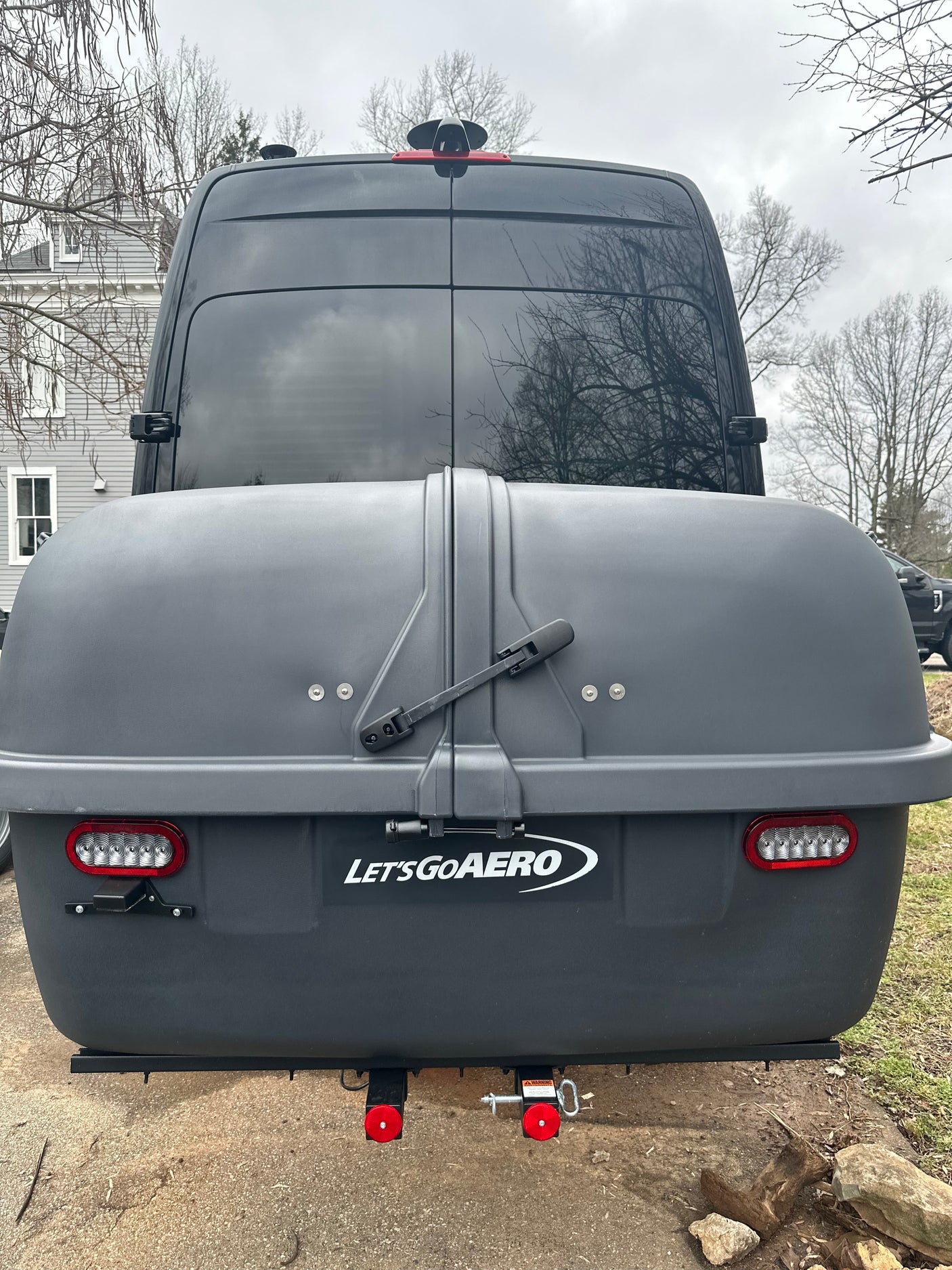 Rear of an RV rental van with a dark "Let's Go Aero" hitch-mounted storage box, showing integrated LED taillights.
