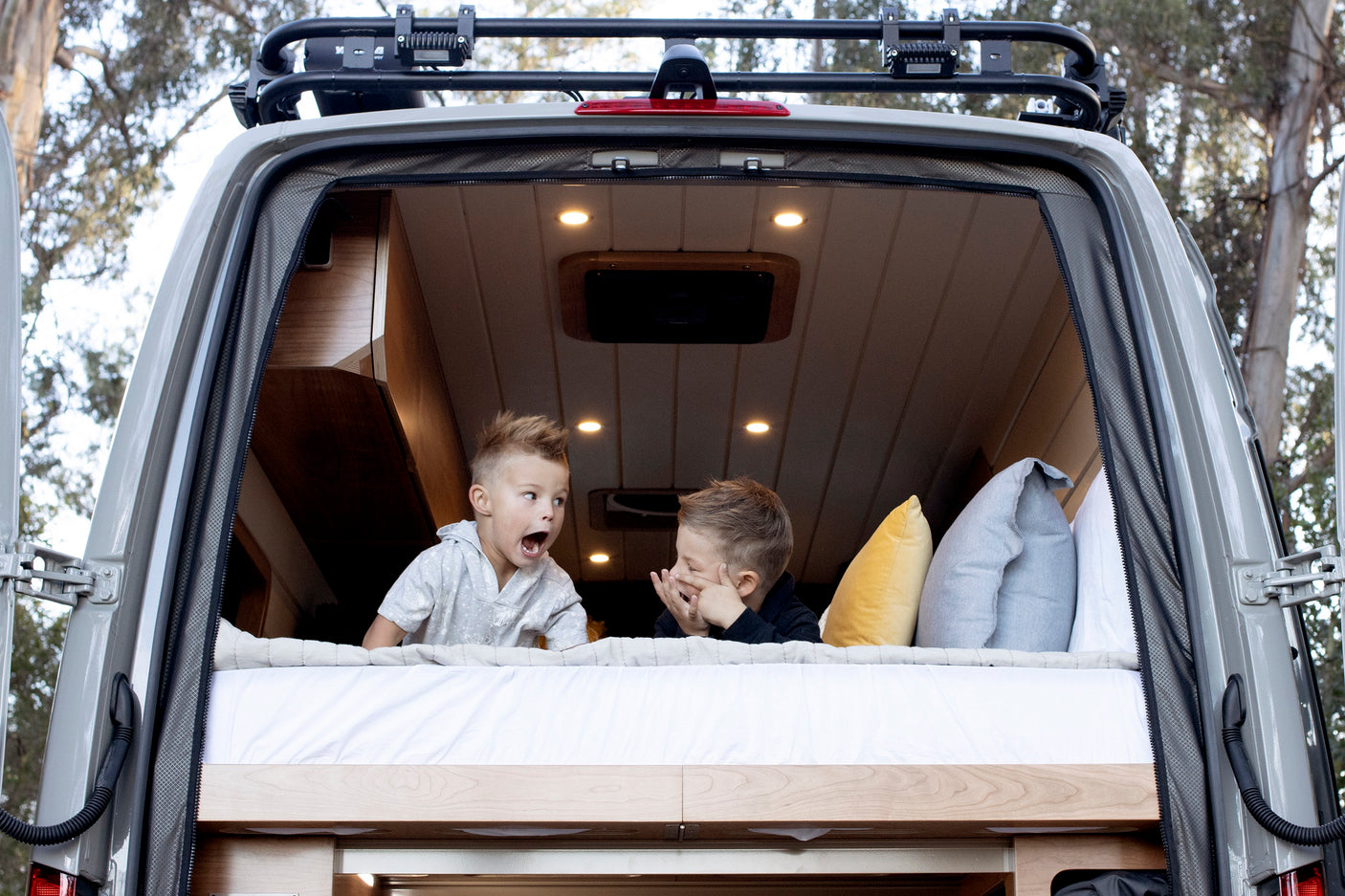 Two kids enjoy an RV rental, playing on the comfy bed in the open back of a camper van. Family adventure awaits!
