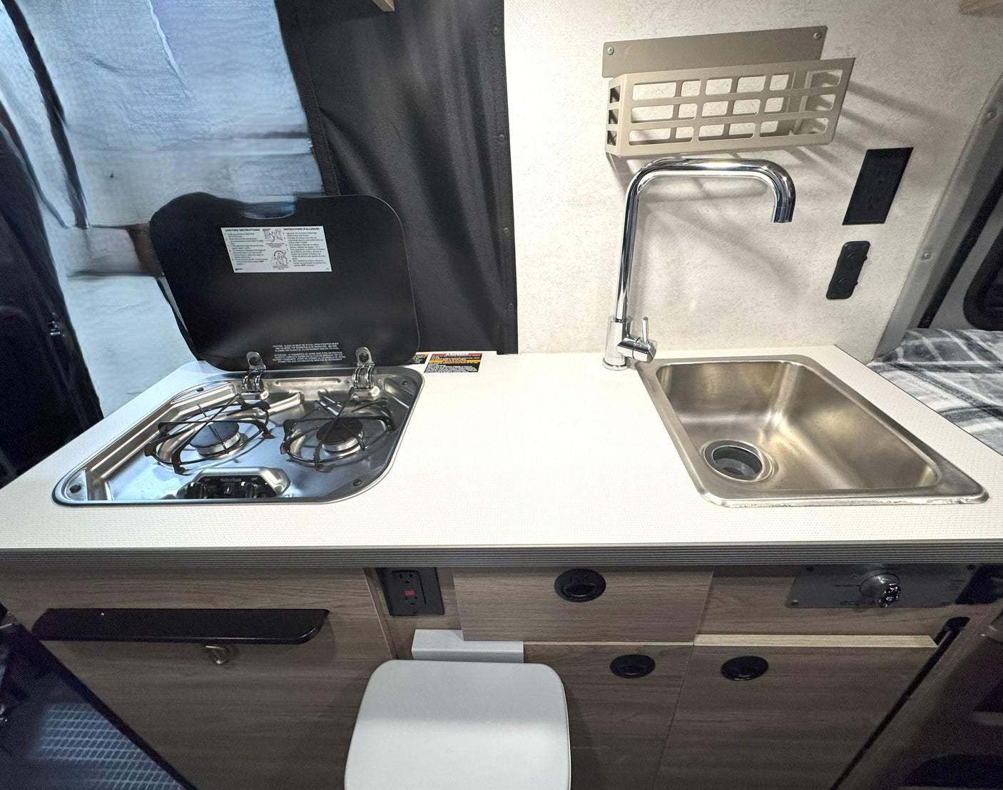 Compact RV rental kitchenette featuring a stove, sink, and counter, with a toilet tucked neatly below.