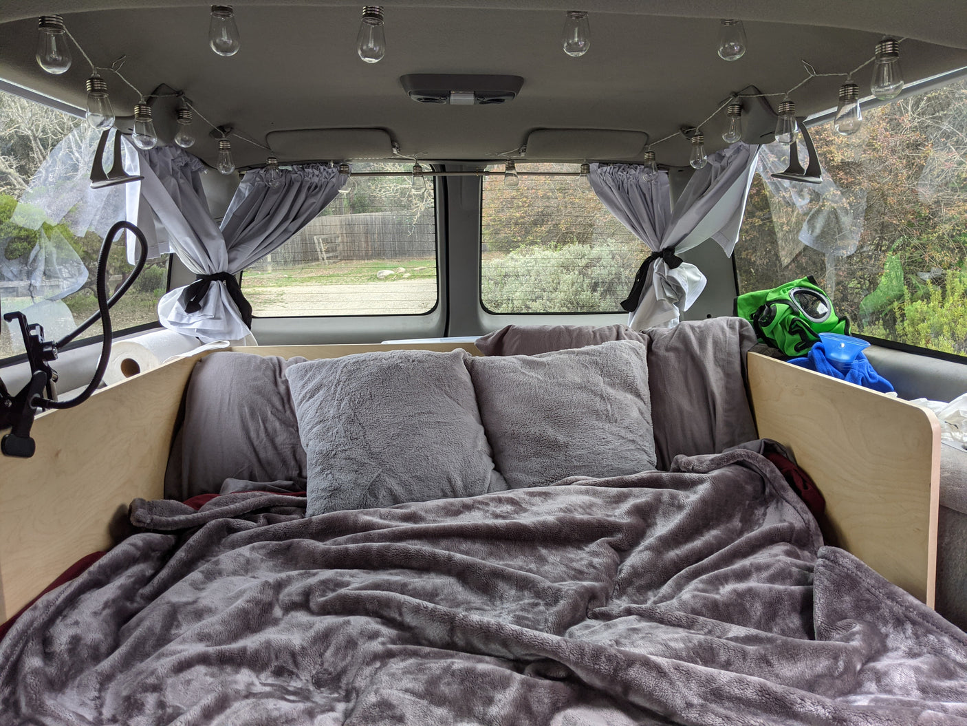 Cozy RV rental bed with string lights & curtains, perfect for comfortable travel inside a customized camper van.