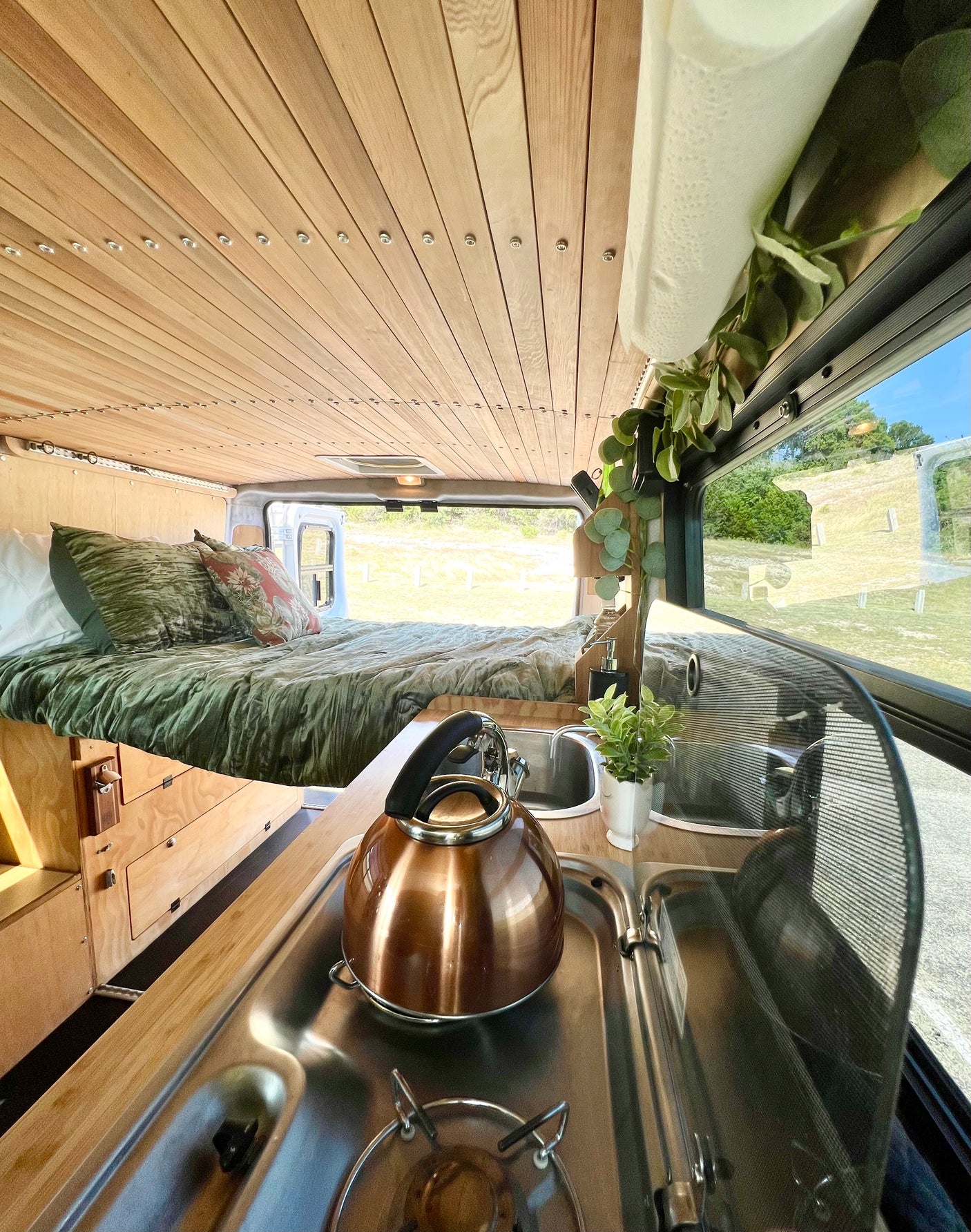 Cozy rv rental interior: wood ceiling, comfy bed, and compact kitchen with a kettle, ready for adventure.
