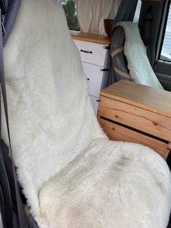 Cozy RV rental interior: plush white sheepskin on a campervan bed/seat, with practical wood crate and cabinets.