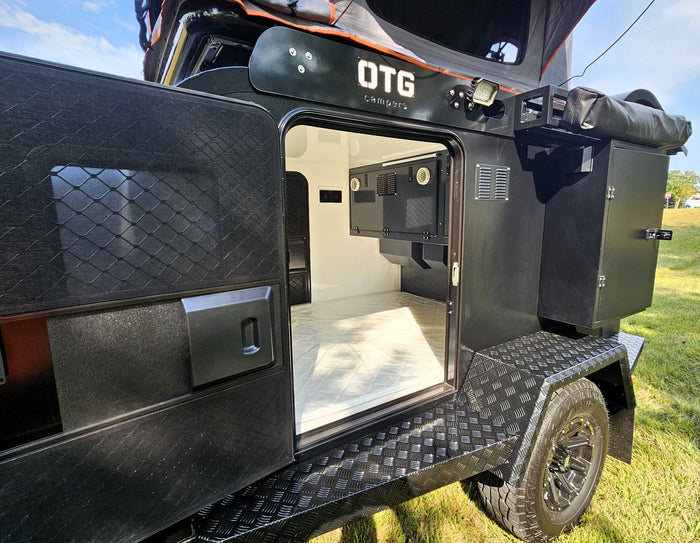 showing open battery storage. Features rugged design & roof-top tent for adventure.|Open door view of a rugged black OTG camper