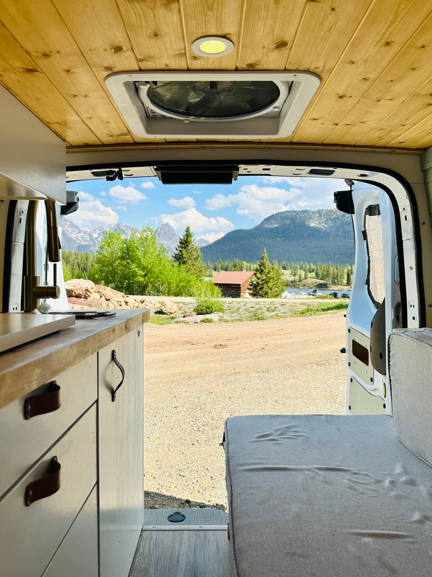 Inside an RV rental van with a comfy bed, kitchen counter, and stunning mountain lake view.