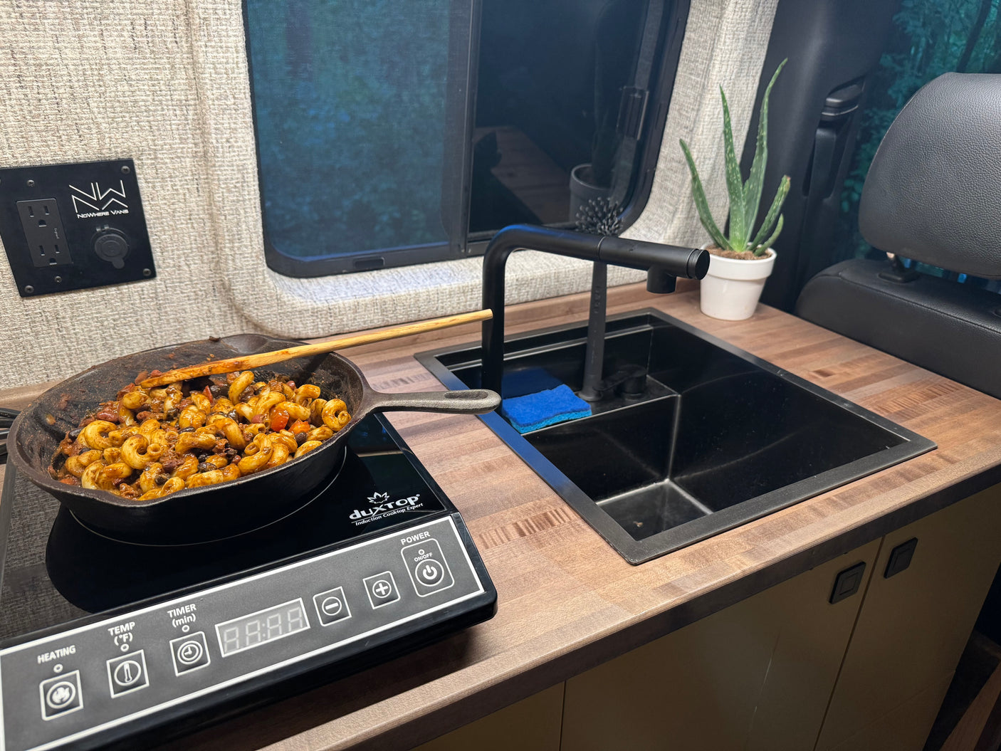 RV rental kitchen scene: Pasta cooking on an induction cooktop. Features a modern sink, counter, and power outlets.