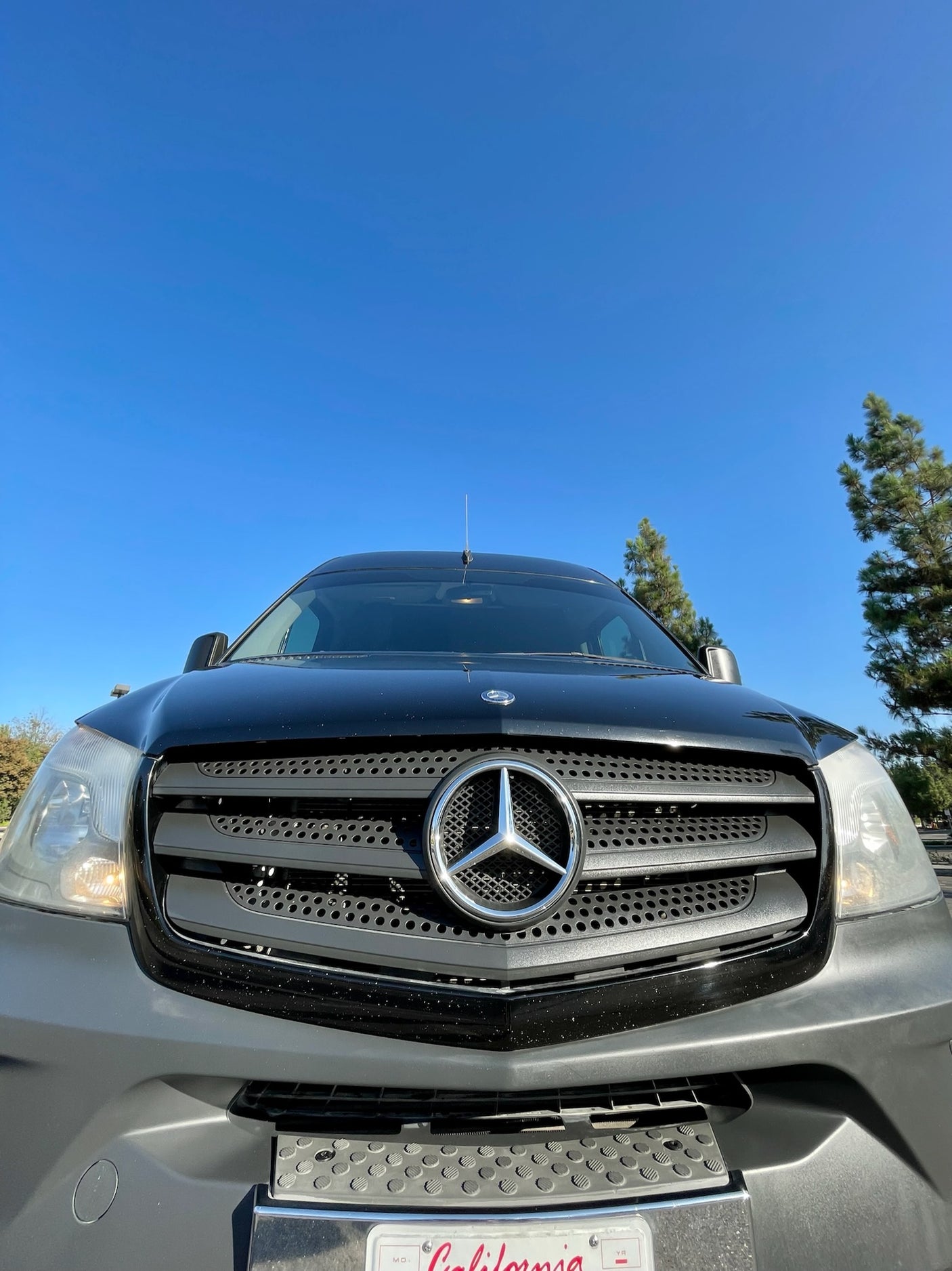 Close-up front view of a black Mercedes-Benz Sprinter van against a clear blue sky, perfect for your rv rental adventure.