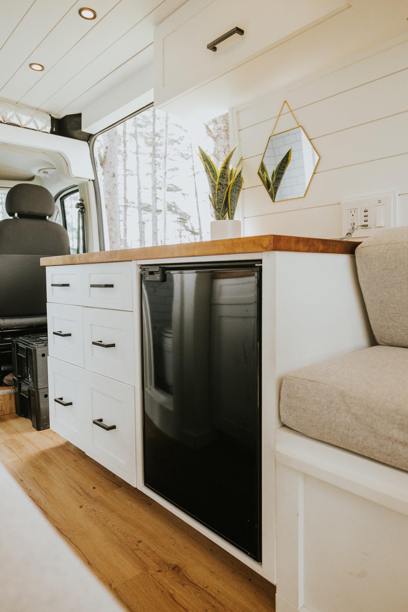 Modern RV rental interior: white shiplap walls, wood counter, built-in fridge, storage drawers, & cozy bench.