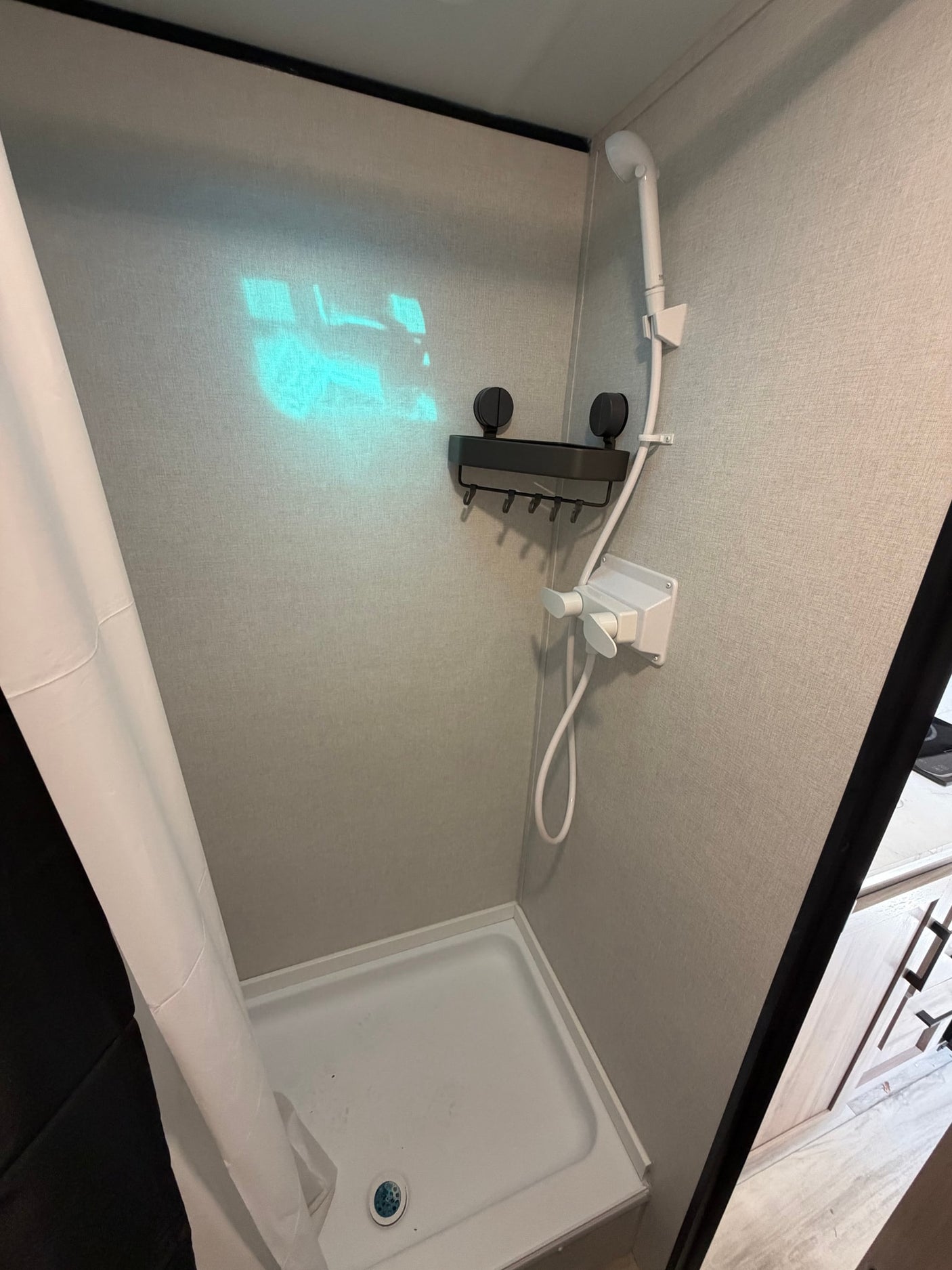Inside an rv rental, this functional shower includes a handheld showerhead, wall caddy, white shower pan, and a curtain.