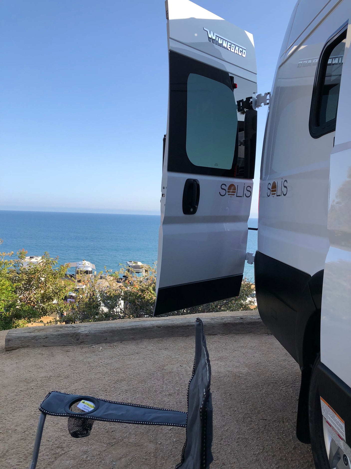 Winnebago Solis rv rental with open doors, offering a serene ocean view from a scenic campsite.
