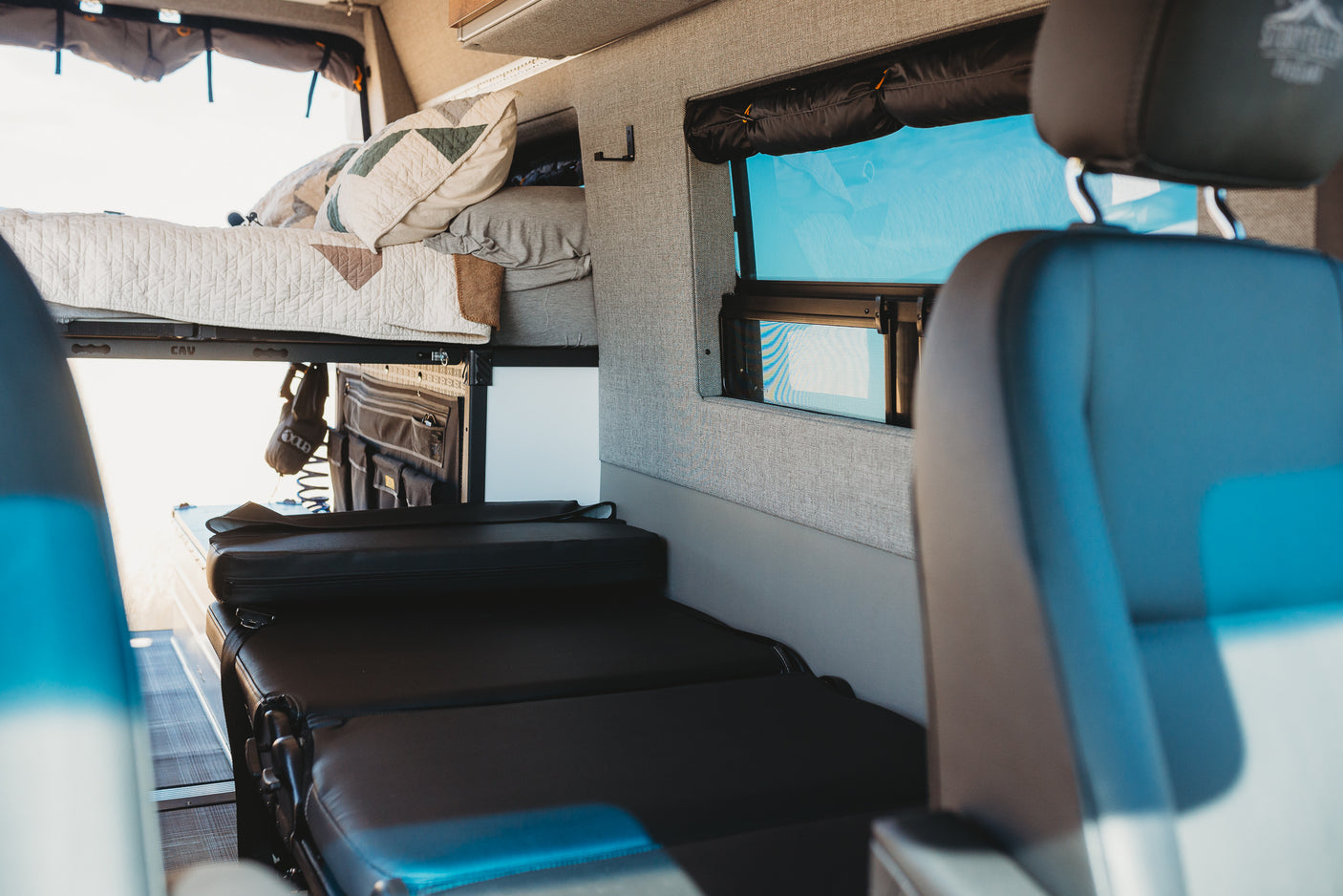 Well-appointed RV rental interior featuring an elevated bed, comfy seating, and window. Ideal for camper travel.