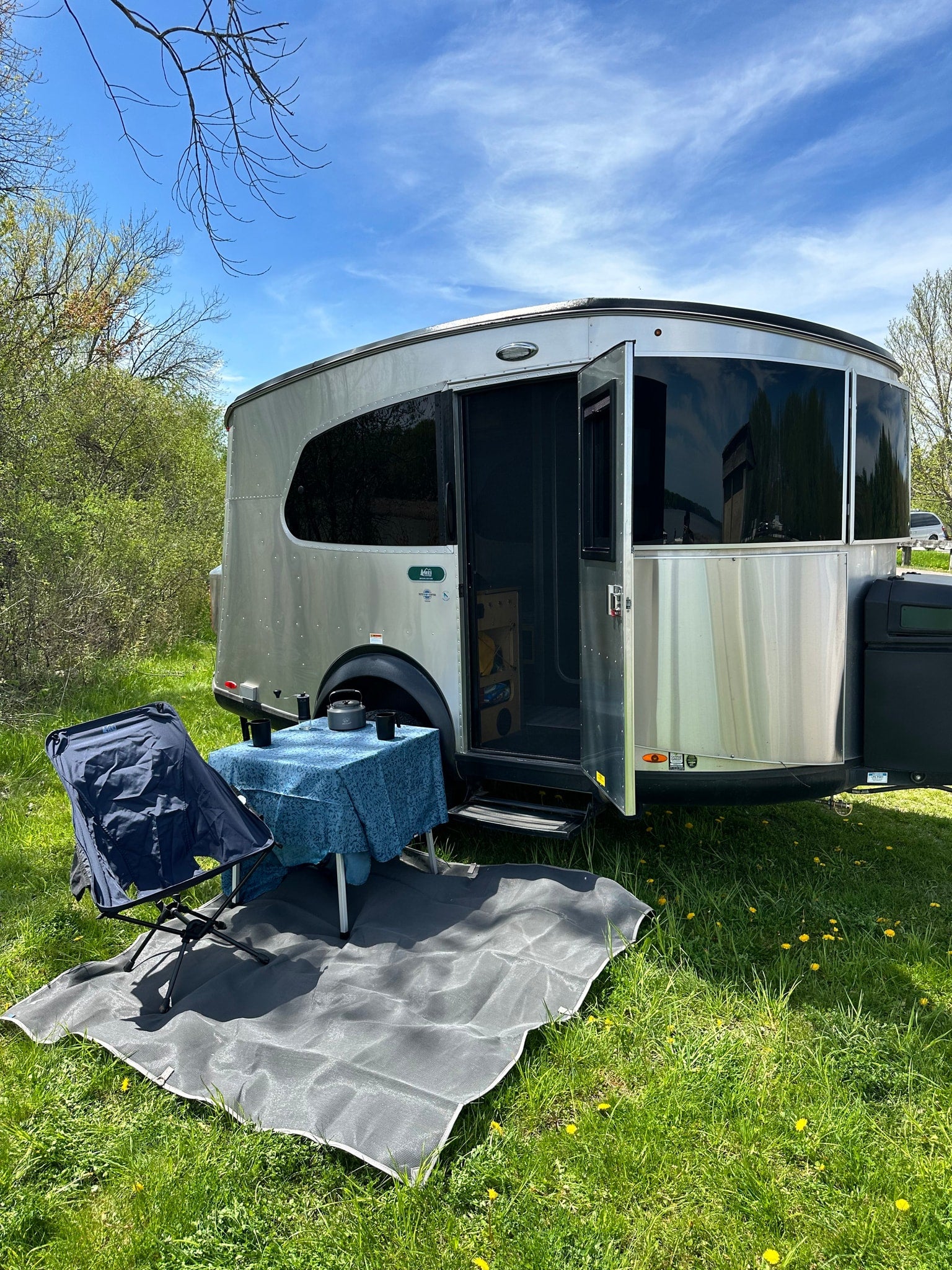 Experience nature in an rv rental: silver travel trailer with an open door, outdoor dining setup on green grass, under a blue sky.