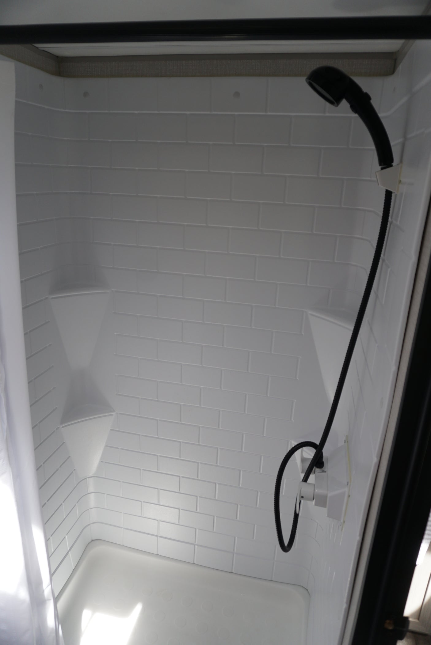 RV rental's bright, compact shower interior with white faux subway tile walls, corner shelves, and a handheld shower.