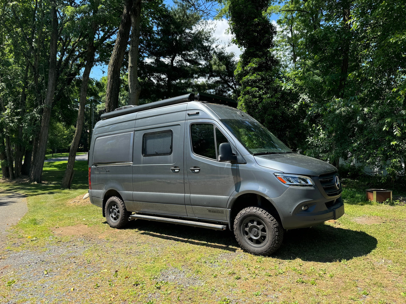 Gray Winnebago Revel RV rental (Sprinter) parked on grass amidst trees. Ready for your next adventure.