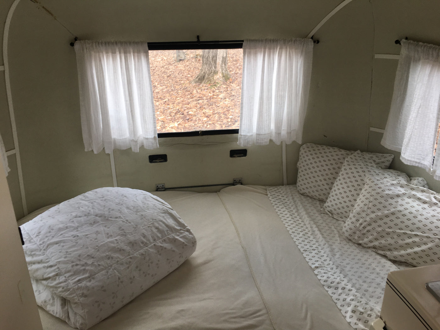 RV rental interior: A cozy bedroom with a white comforter, patterned pillows, and a window overlooking a leafy forest. — photo 8