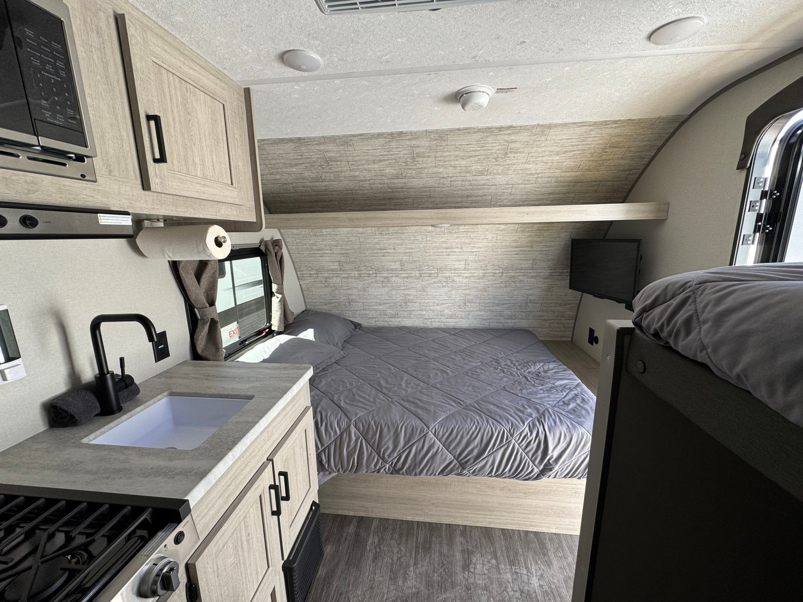 Inside this modern RV rental, find a compact kitchen with microwave, sink, and stovetop, plus a queen bed and bunk.
