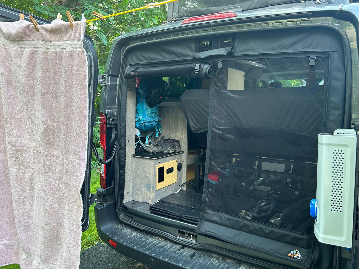 RV rental camper van setup: Back doors open revealing custom interior, bug screen, and clothesline. Ideal for van life.