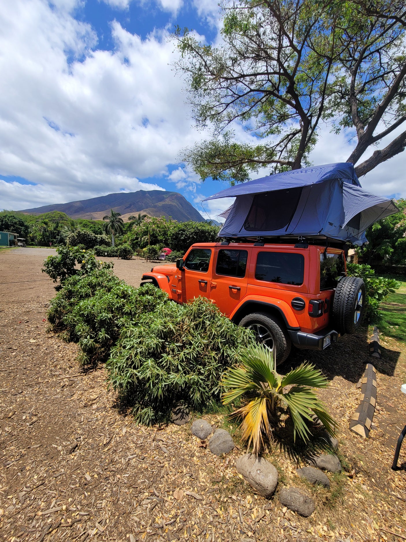 An orange Jeep Wrangler with an open blue rooftop tent, offering a unique RV rental experience in a natural, mountainous landscape.