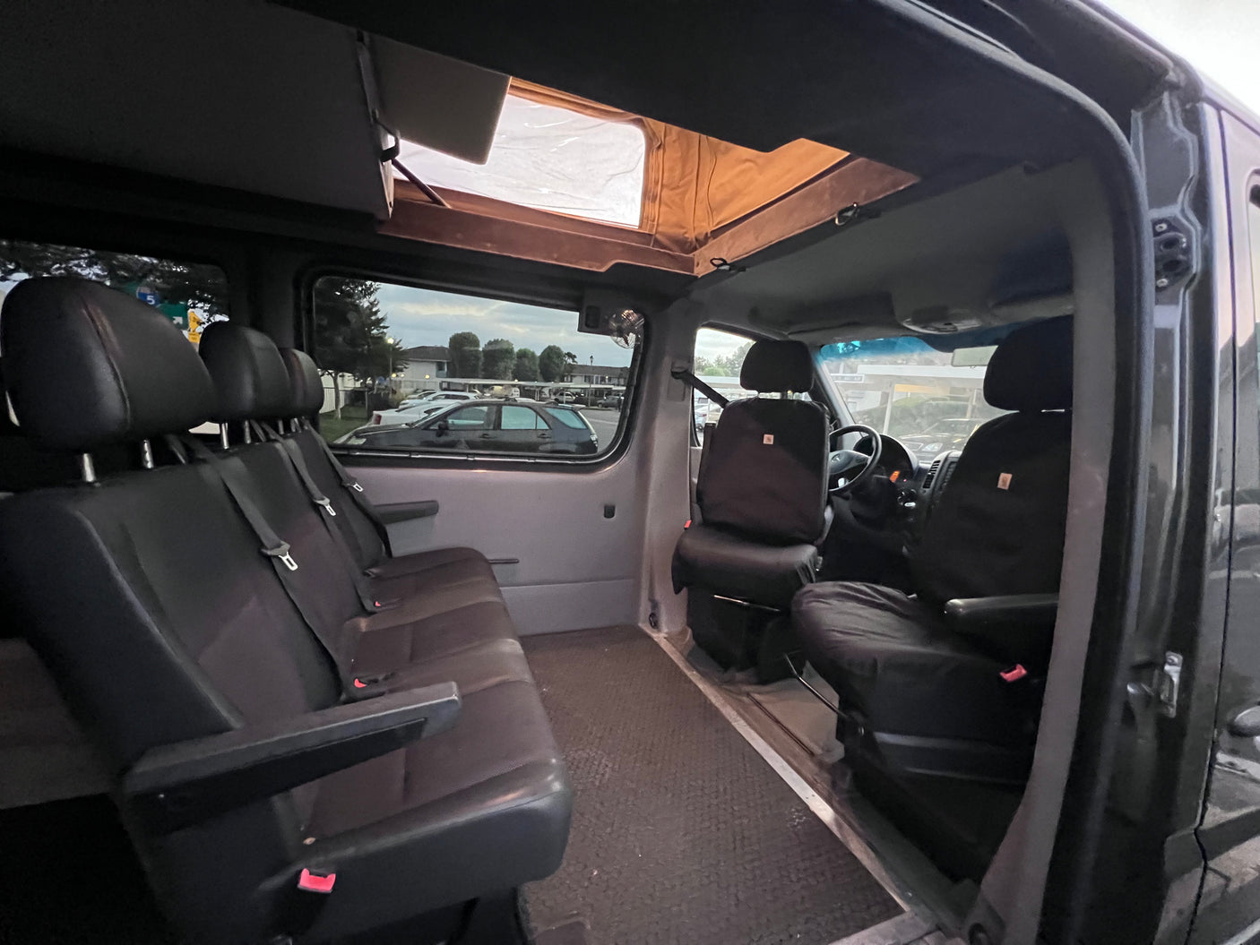 RV rental interior featuring black seating, a driver's area, and an open pop-top roof for light.
