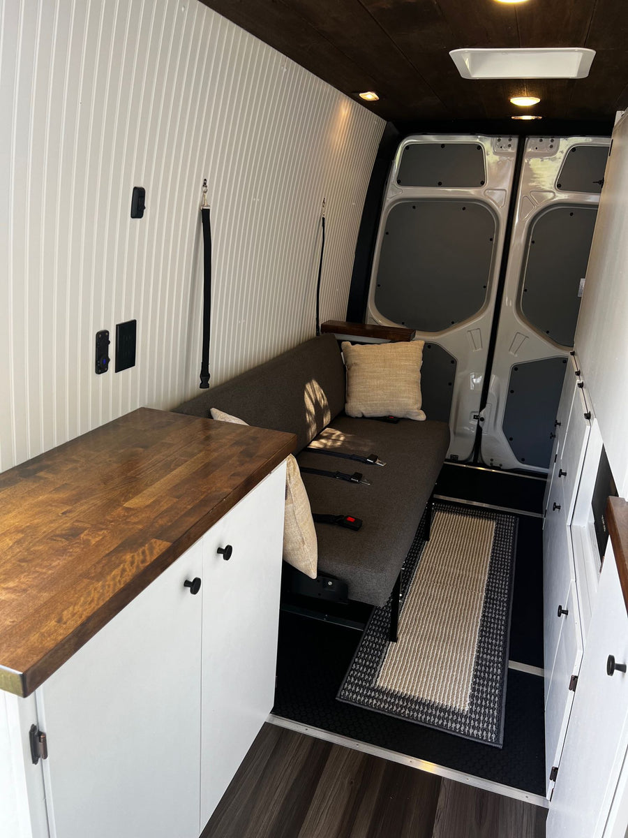 and front cabin view of a camper van.|This RV rental interior showcases a modern kitchen with white cabinets