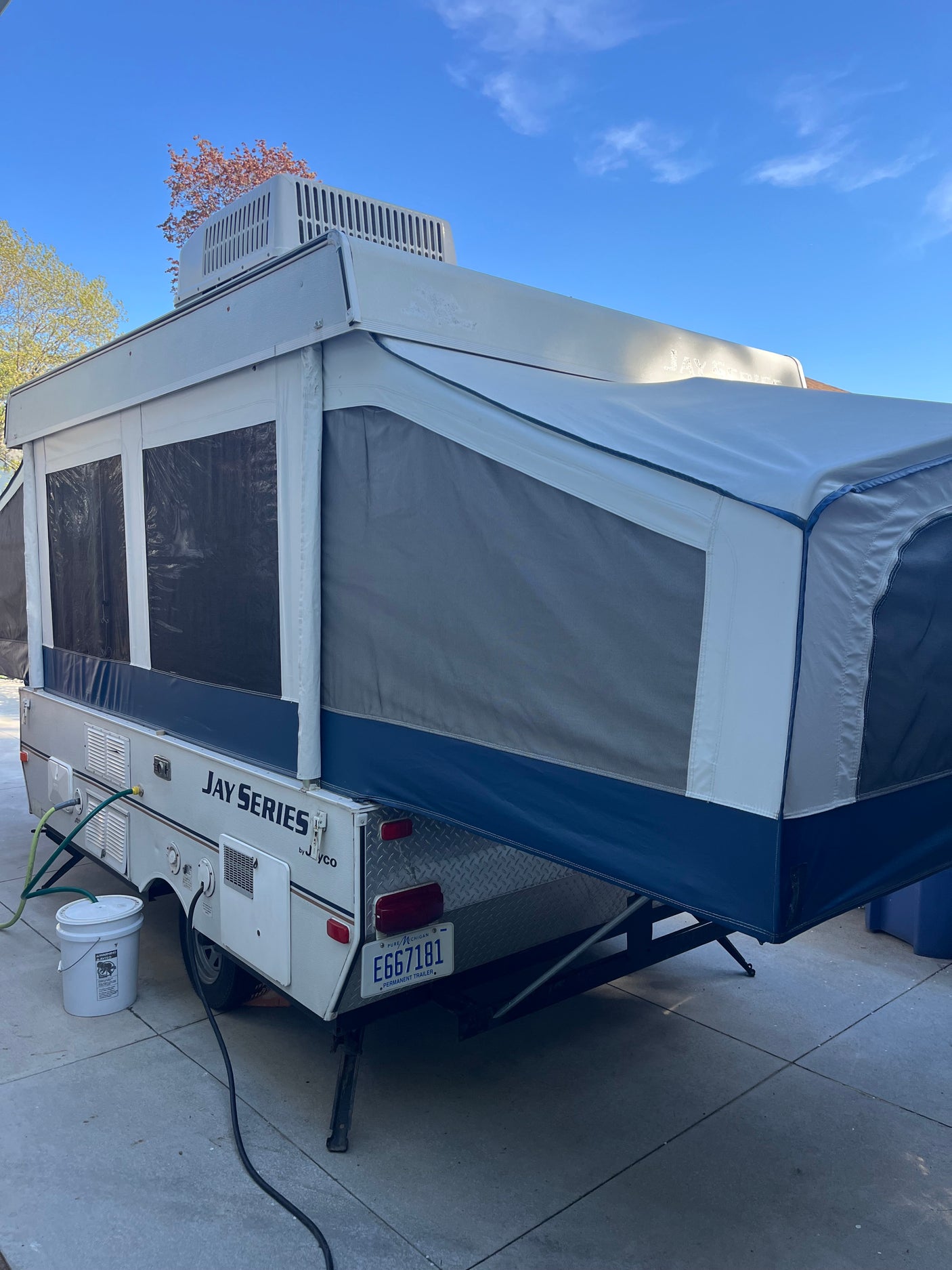 Fully extended Jayco pop-up camper in white/gray/blue, hooked up on a paved lot. Great RV rental!