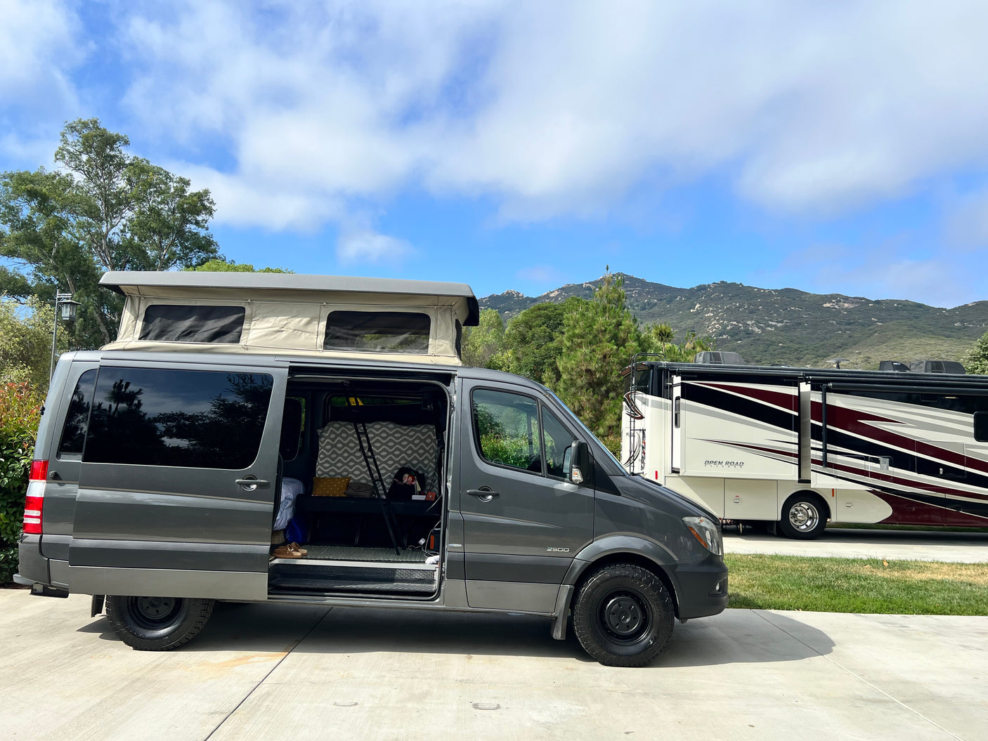 Grey Sprinter camper van with pop-top next to an RV, perfect for your next RV rental adventure in the mountains.