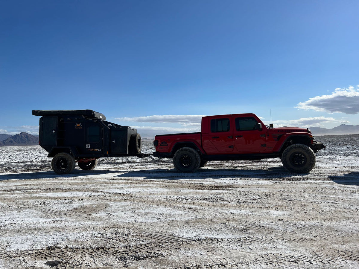 Red Jeep truck with an overland trailer in a vast dry landscape. Your ultimate RV rental for off-road expeditions!|Black