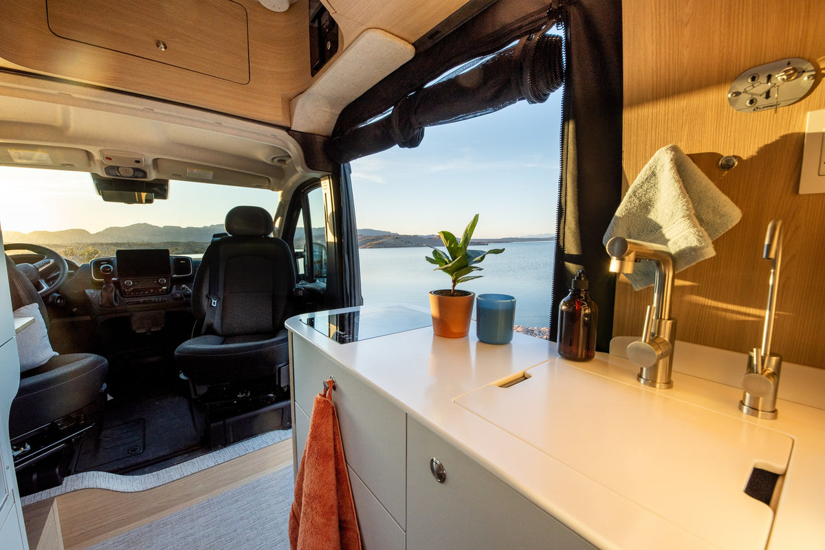 Inside a modern rv rental camper van, showing a kitchenette, cockpit, and stunning lake and mountain views through the open door. — photo 8