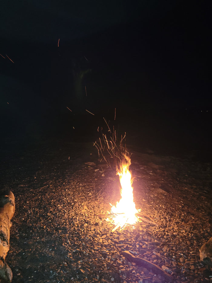 A vibrant bonfire illuminates a pebbled ground at night, with sparks rising. Ideal camping moment with your RV rental.
