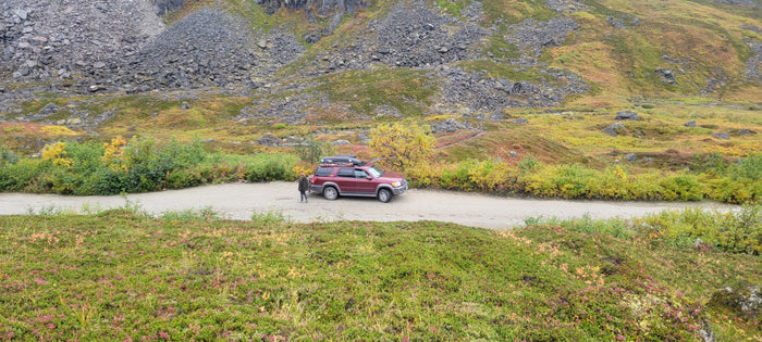 Maroon SUV on a dirt road in fall mountains, great for exploring. Consider an rv rental for similar scenic adventures!