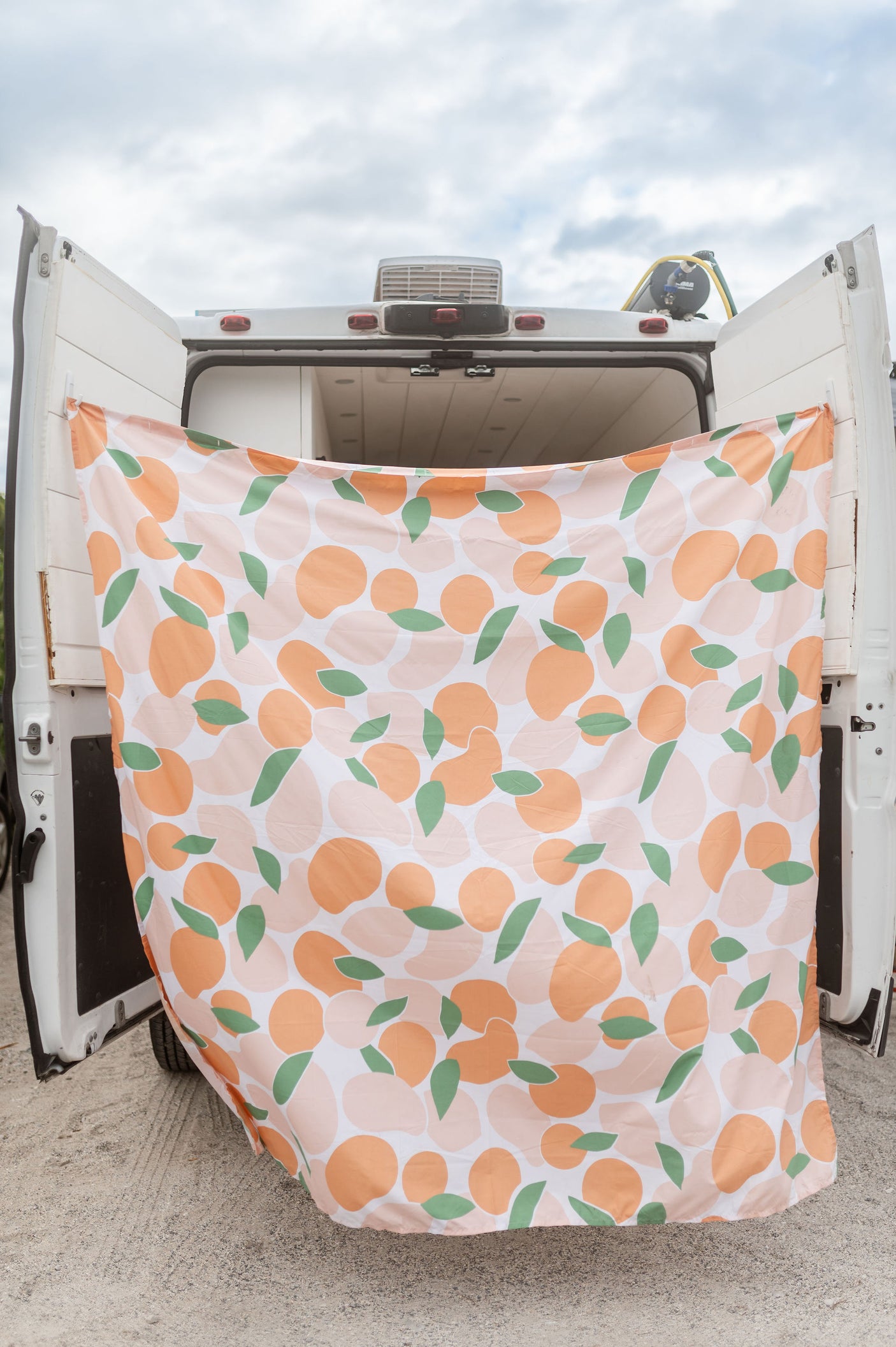 White RV rental with open rear doors. A vibrant peach and leaf patterned curtain hangs, creating a private outdoor space.