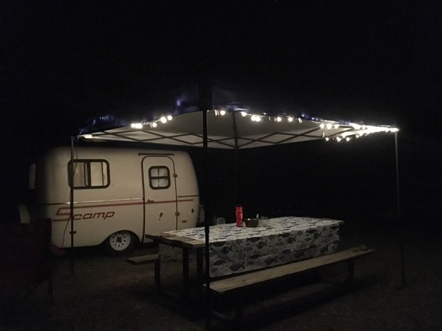 Cozy night camping with a small travel trailer rental, lit canopy, and picnic table at a campsite. — photo 9