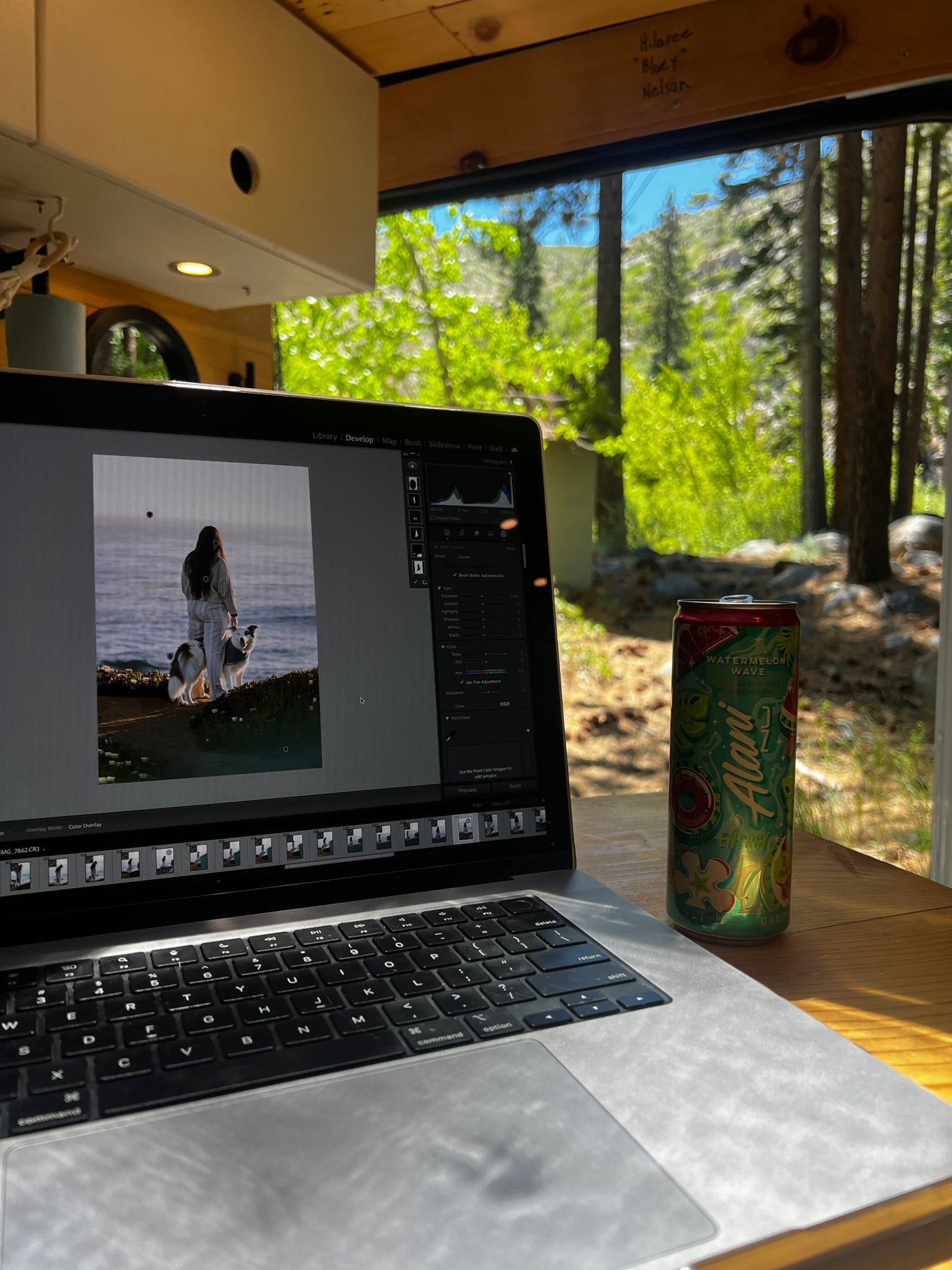 Enjoying remote photo editing in an RV rental, with a scenic forest view and an energy drink nearby.