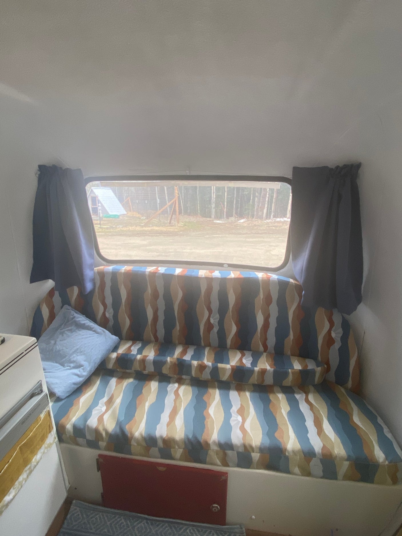Cozy rv rental interior featuring a patterned bench/bed, window view of trees, and blue pillow. Ideal for comfortable travel.