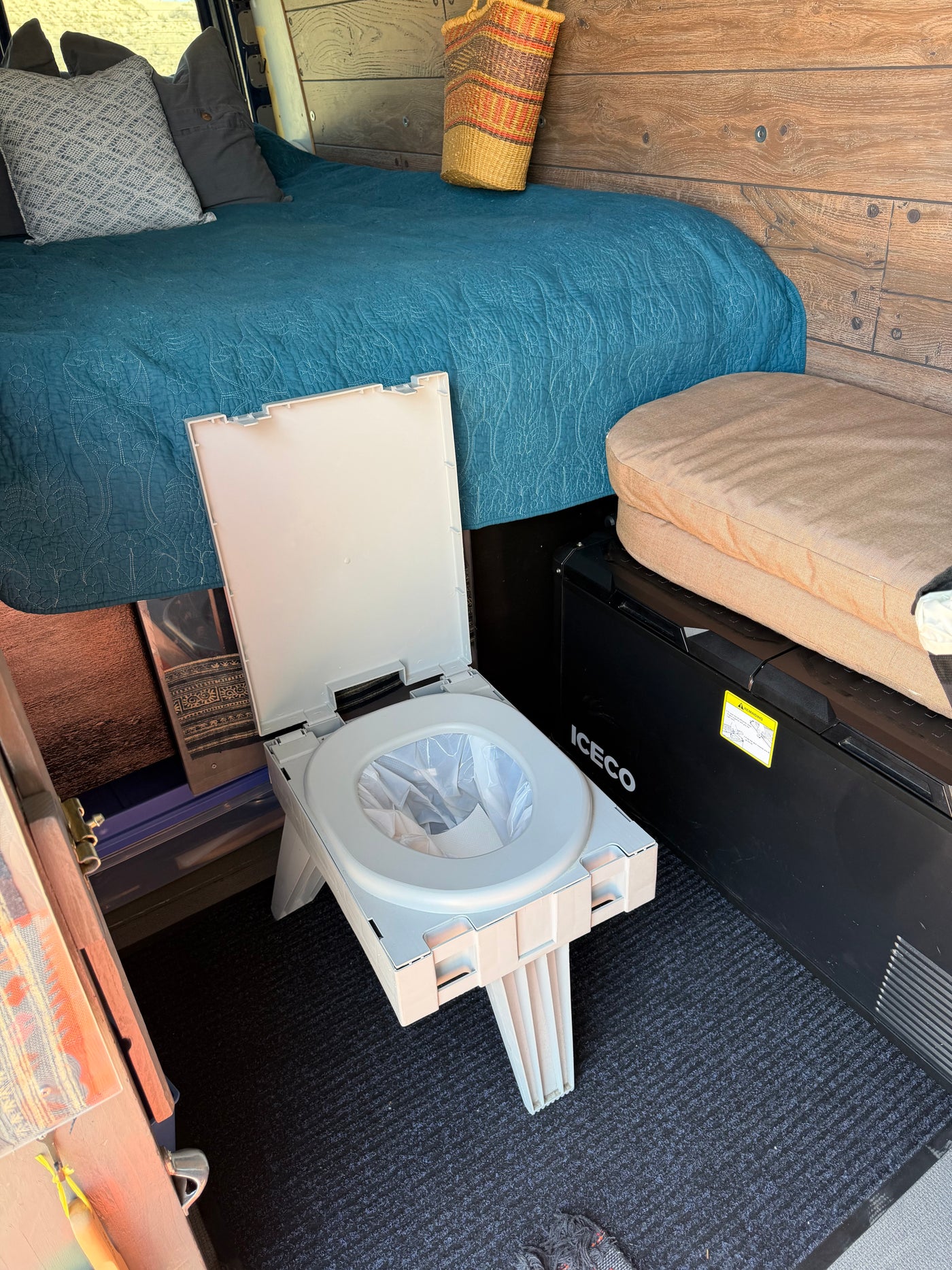 Portable camping toilet with liner in an rv rental camper van interior, next to a bed and fridge. Ready for adventure. — photo 11