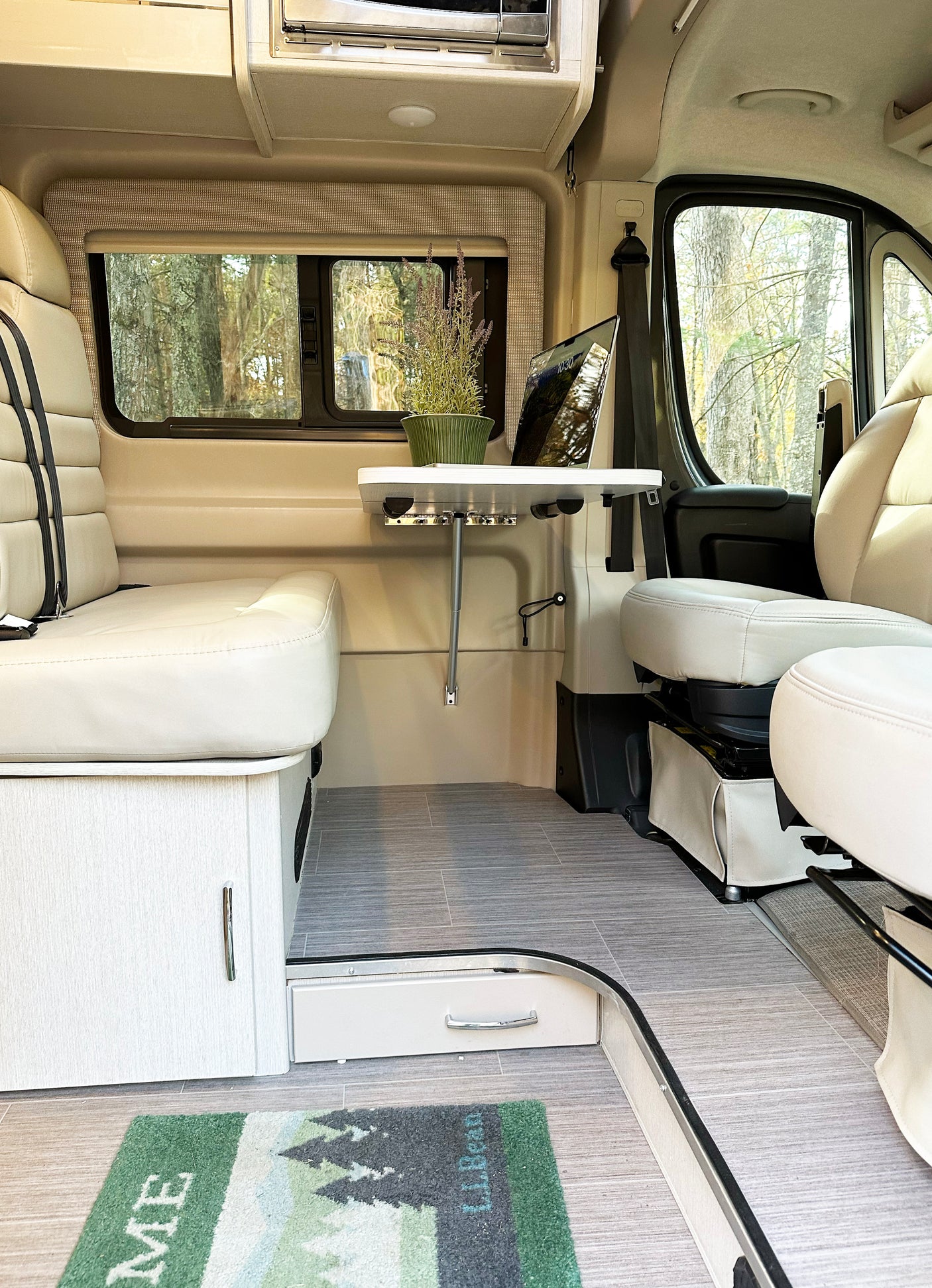 Inside this modern rv rental: light seating, wood-look cabinets, a table for work, and panoramic nature views. Spacious and bright.