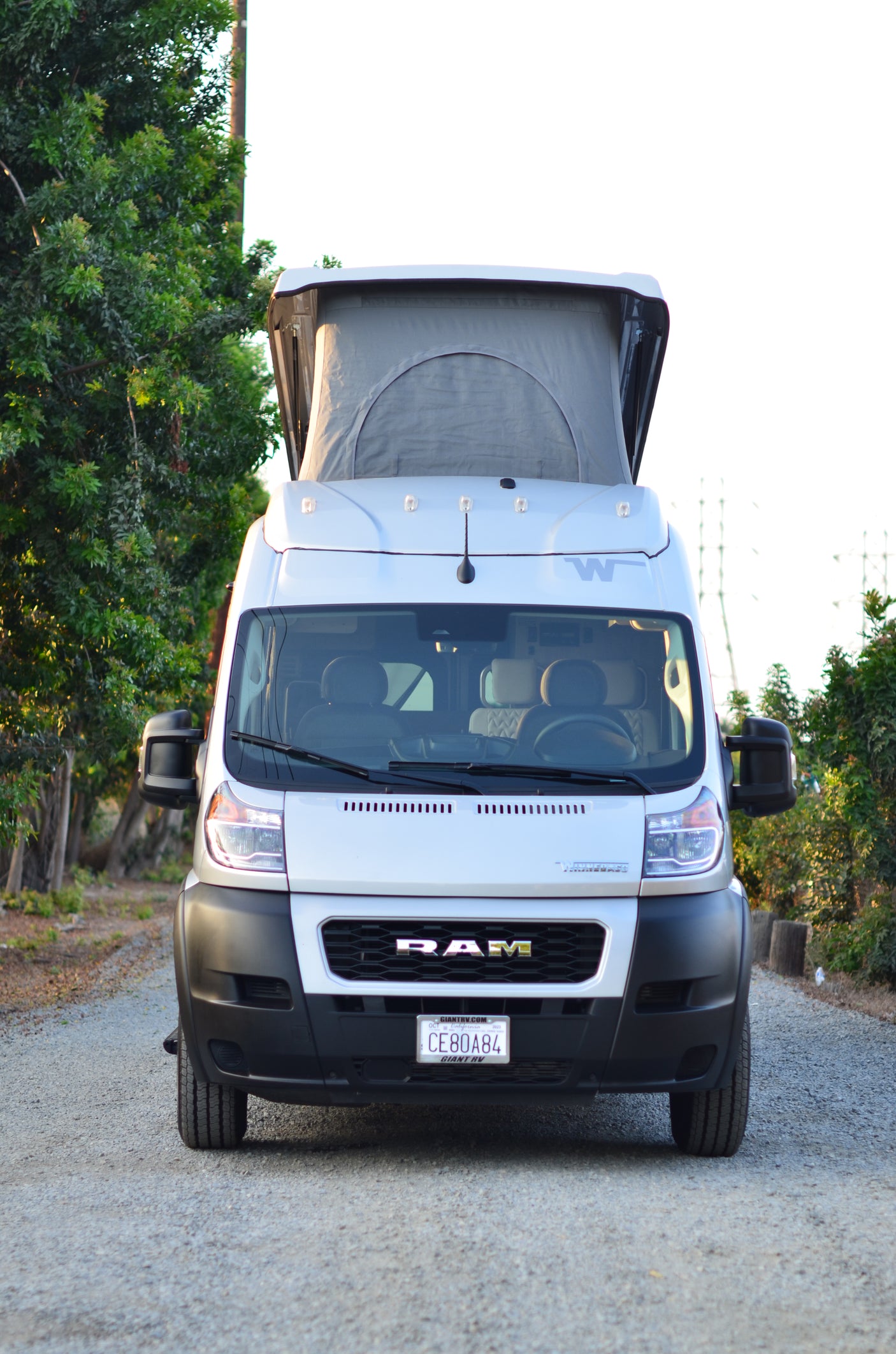 White RAM pop-top camper van, an rv rental, with its roof extended. Parked on asphalt, ready for outdoor adventures.
