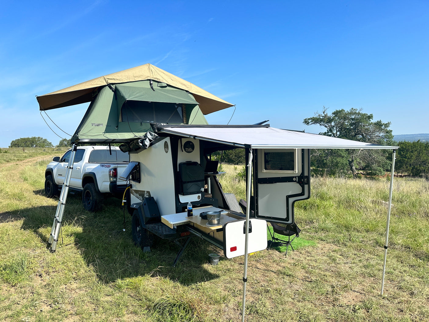 This RV rental overland setup features a truck with a rooftop tent & an equipped off-road trailer, perfect for outdoor camping.