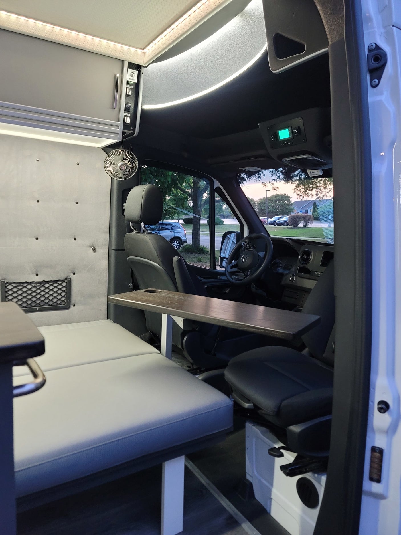 parked on a tree-lined road. Nature setting.|White Mercedes-Benz Sprinter RV rental parked on grass by a sandy beach with the ocean/lake at dusk. Scenic travel van.|White Mercedes Sprinter RV rental van