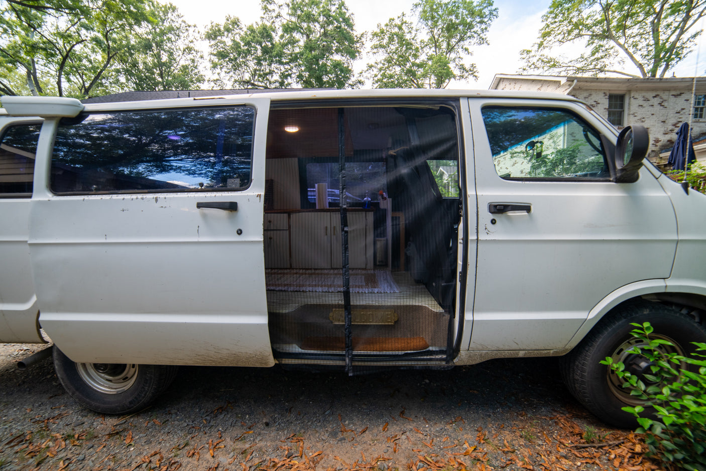 White camper van RV rental, side door open to a cozy interior with kitchenette and screen. Ready for adventures!