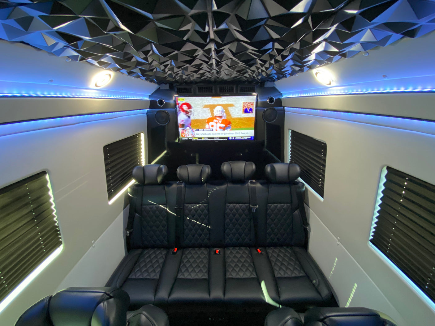 Spacious luxury rv rental interior featuring custom black seating, a large TV for football, and stylish blue LED lights.
