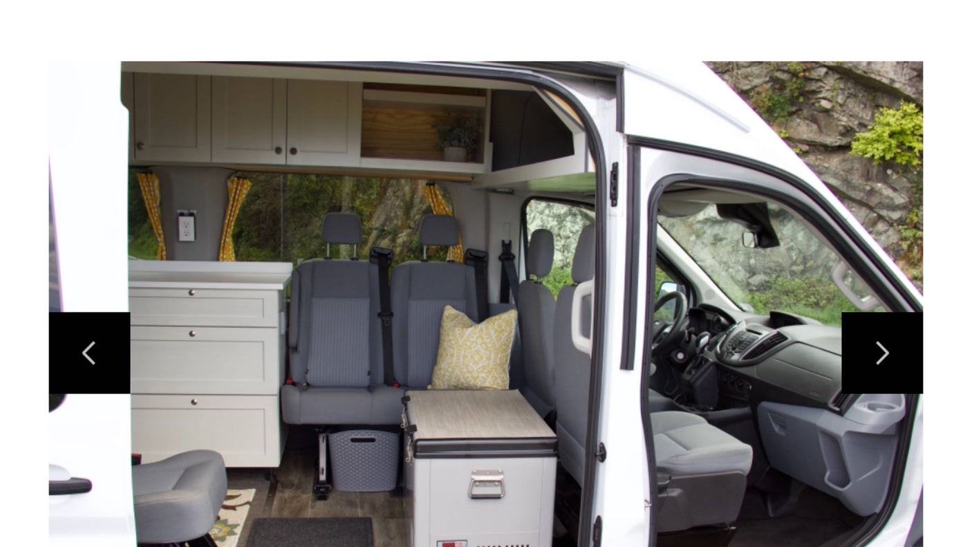 at a scenic riverside campsite surrounded by lush green trees.|Compact RV rental interior featuring custom storage
