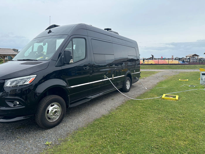 ready for adventure.|Black RV rental van hooked up at a campground. People enjoy an inflatable in the background under an overcast sky.|rv rental interior featuring dark wood overhead cabinets