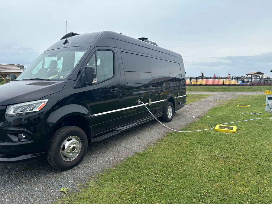 ready for adventure.|Black RV rental van hooked up at a campground. People enjoy an inflatable in the background under an overcast sky.|rv rental interior featuring dark wood overhead cabinets