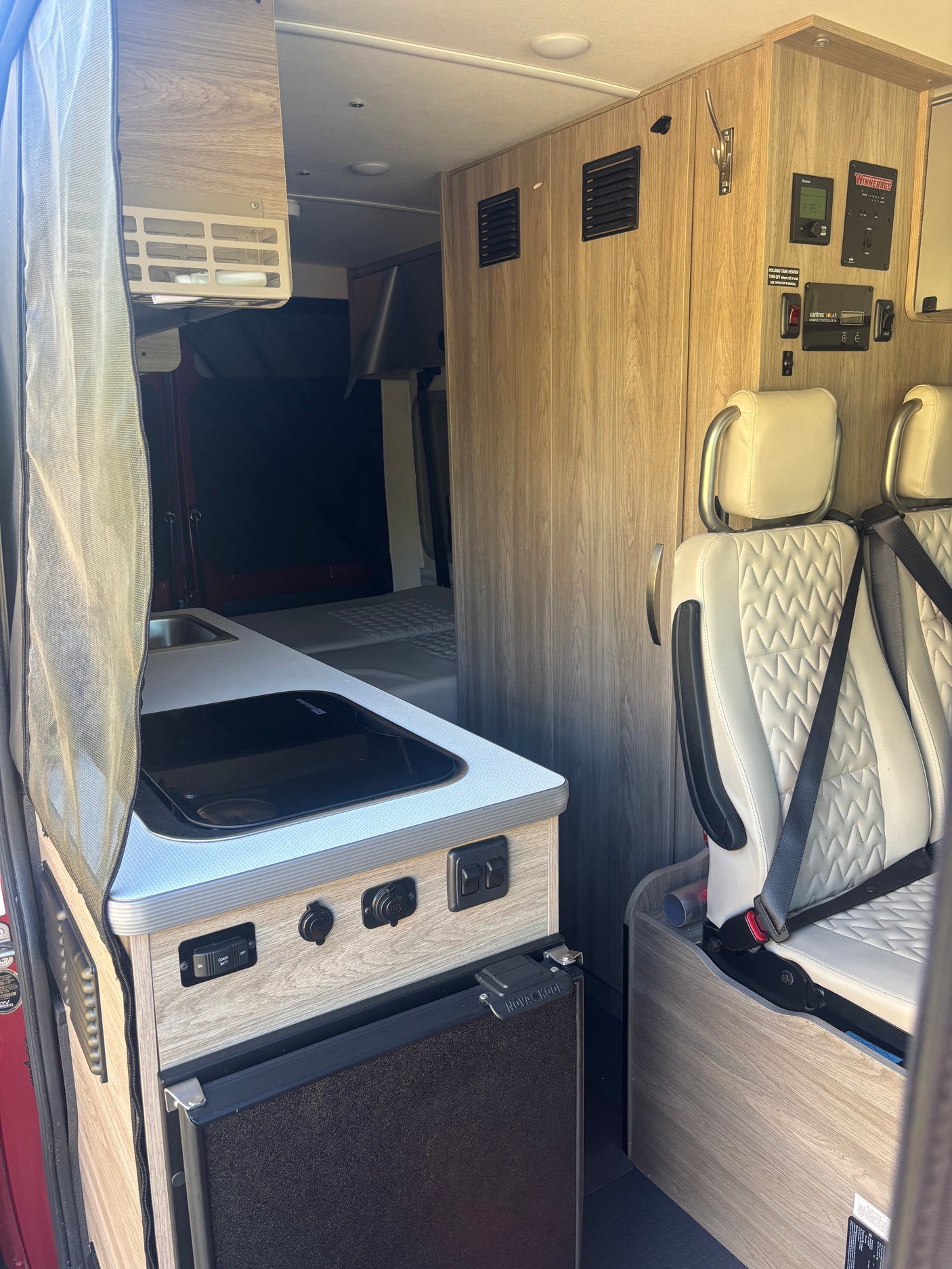 RV rental interior view: built-in kitchenette, fridge, Winnebago control panel, and passenger seats, ready for adventure.