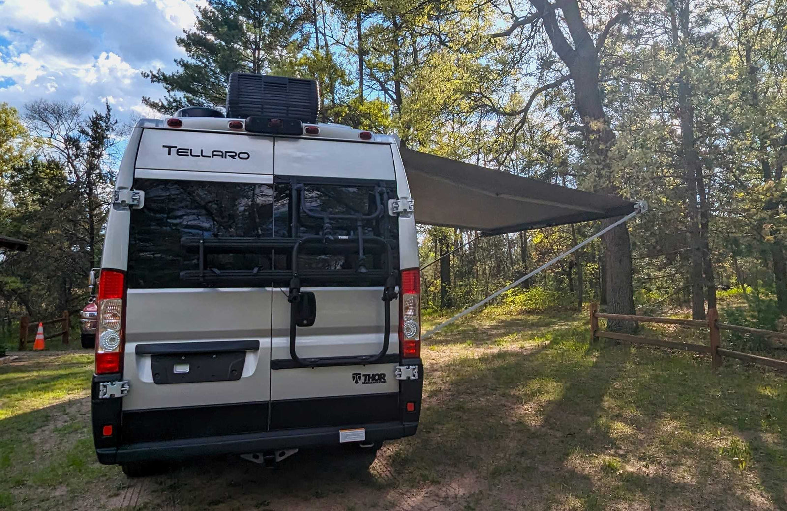 is parked beside a tranquil lake under a blue sky with fluffy clouds.|Grey rv rental camper van