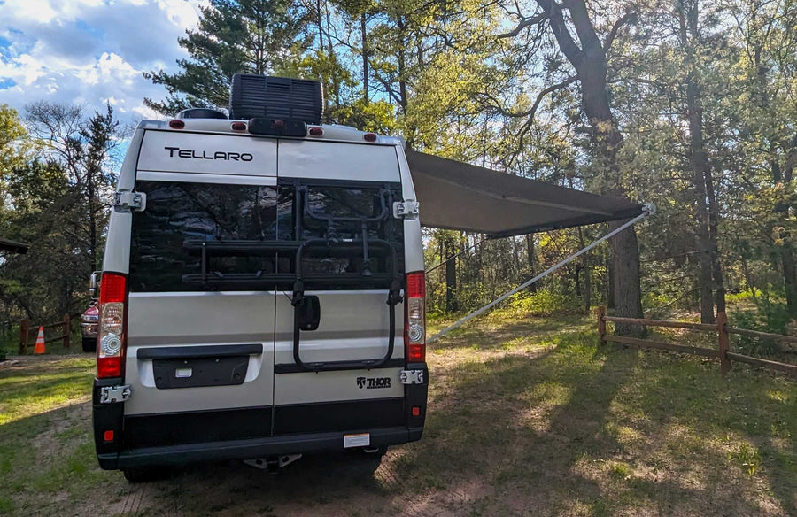is parked beside a tranquil lake under a blue sky with fluffy clouds.|Grey rv rental camper van