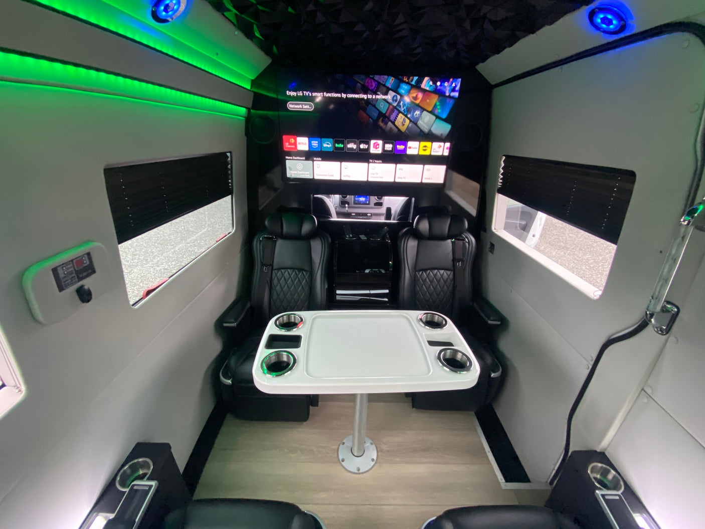Luxury RV rental interior features black leather captain's chairs, a table with cupholders, smart TV, and ambient LED lighting.