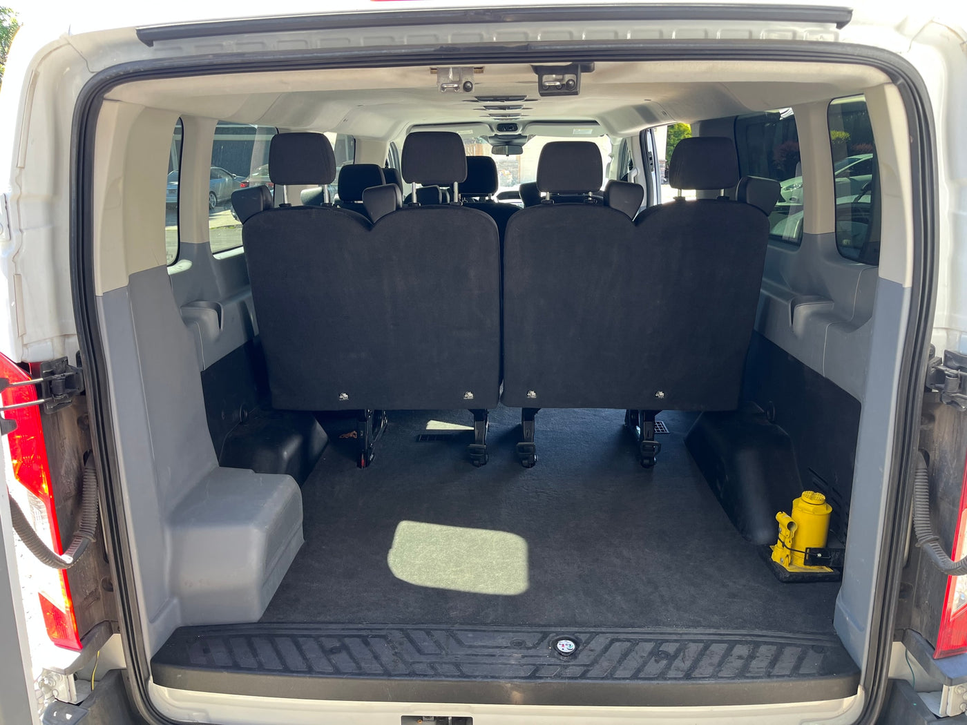 Inside a white passenger van for RV rental, showing two rows of black seats, cargo space, and a yellow jack at the rear. — photo 5