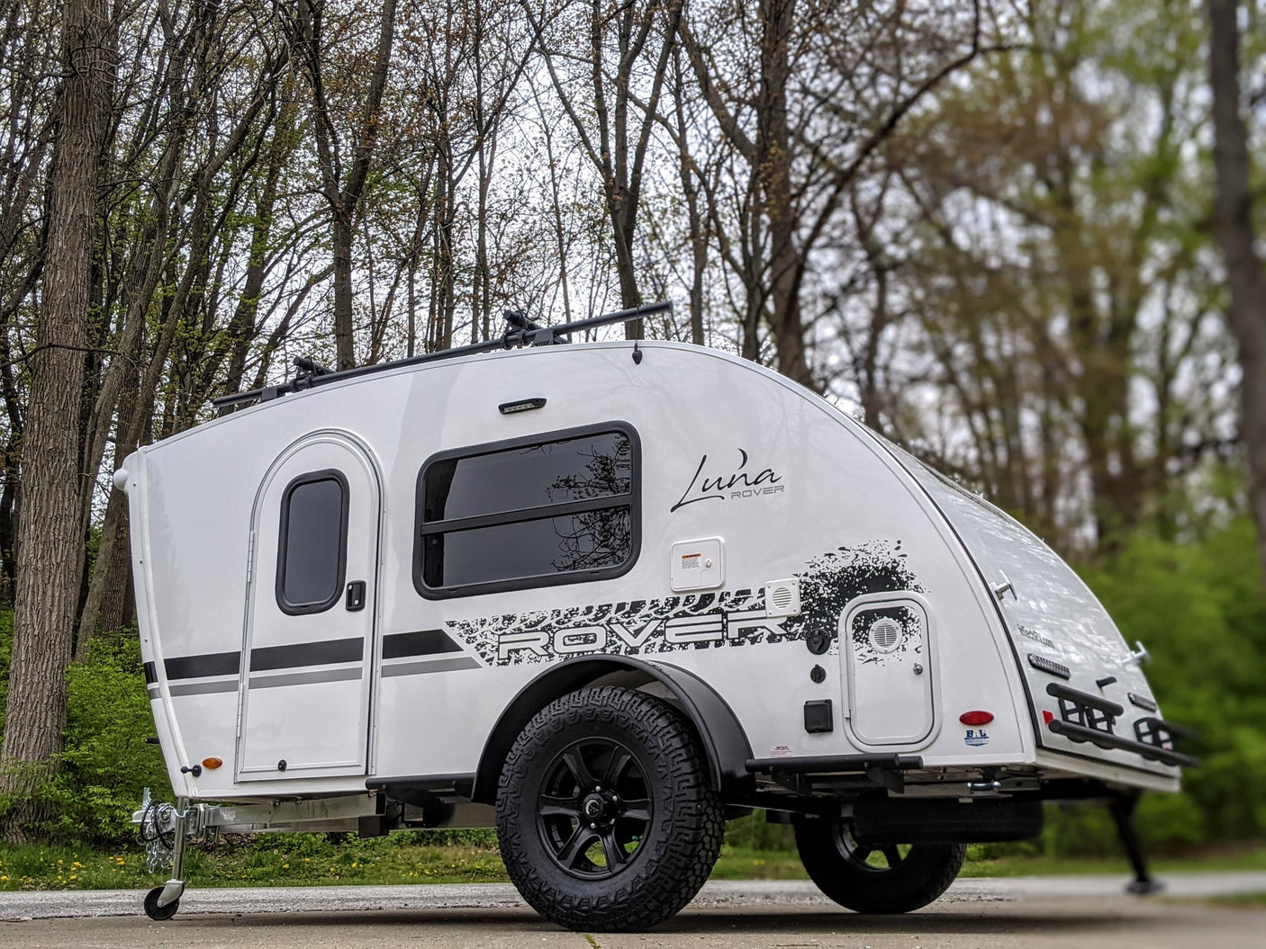 This white Luna Rover teardrop camper, featuring off-road tires and a roof rack, is ideal for your next RV rental adventure.
