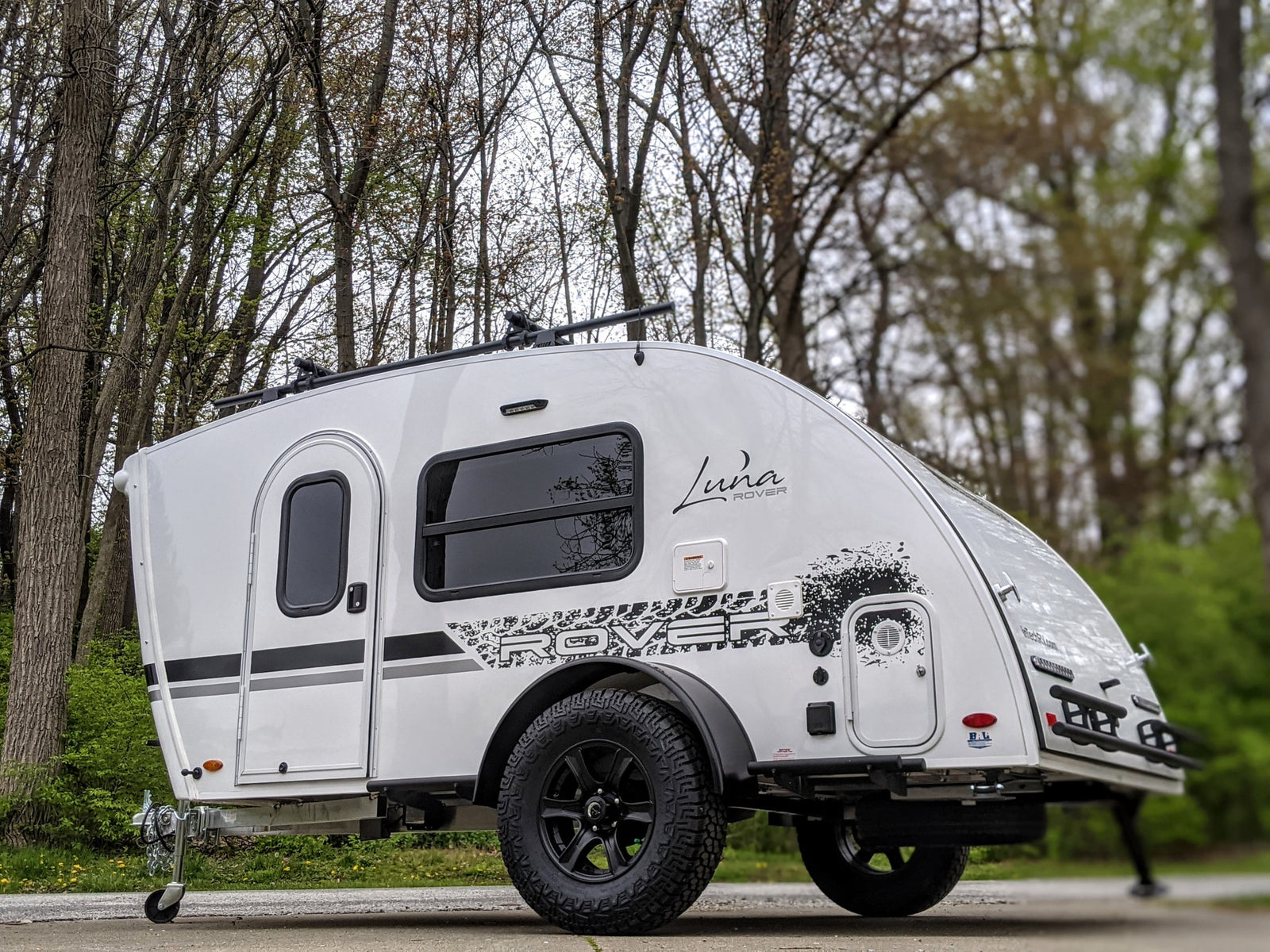 This white Luna Rover teardrop camper, featuring off-road tires and a roof rack, is ideal for your next RV rental adventure.